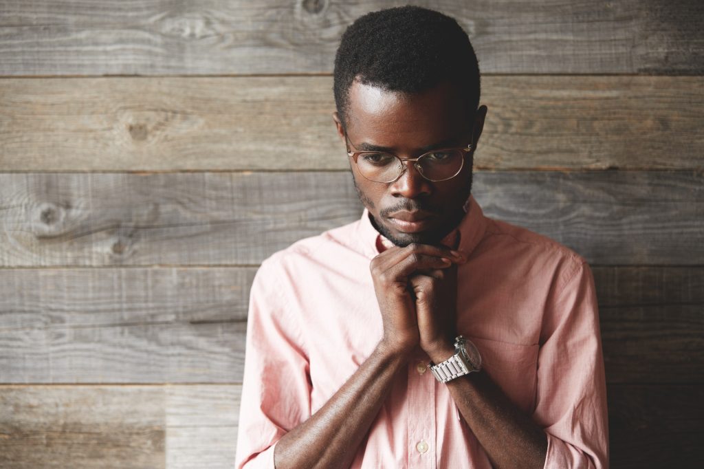 Close up shot of handsome young African man praying and meditating against wooden background. Dark s